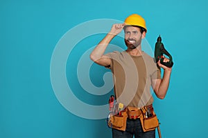 Professional builder in hard hat with tool belt and power drill on light blue background, space for text
