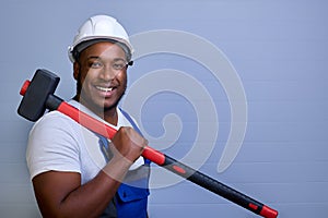 Professional builder in a helmet and work clothes holds a powerful hammer on his shoulder.