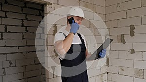 Professional builder holding paper folder with documents and talking on phone.