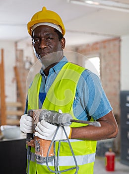 Professional builder holding pneumatic chipping hammer in building under construction