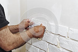 A professional builder installs a new white decorative brick on the wall, close-up