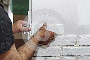 A professional builder installs a new white decorative brick on the wall, close-up