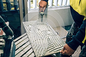 Professional builder smears cement glue on the ceramic tile with a trowel. Concept renovation repair, overhaul, contract