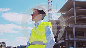 Professional builder standing in front of construction site. Foreman in hardhat helmet and vest. Office building and