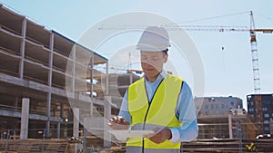 Professional builder standing in front of construction site. Foreman in hardhat helmet and vest. Office building and