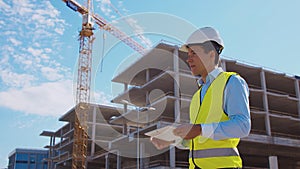 Professional builder standing in front of construction site. Foreman in hardhat helmet and vest. Office building and