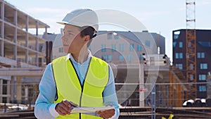 Professional builder standing with tablet computer in front of construction site. Foreman in helmet and vest. Office