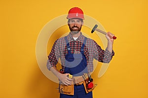 Professional builder in uniform with hammer and tool belt on yellow background