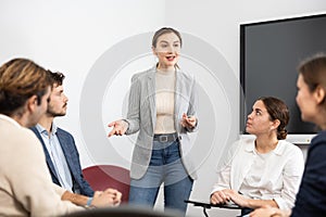 Professional business coach woman standing near interactive board and conducting training different people gathered in
