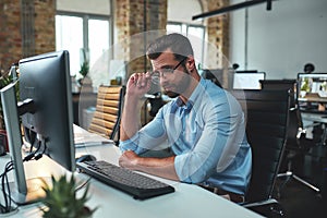 Professional business expert. Young bearded man in formal wear adjusting his eyeglasses and looking at computer while