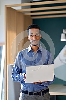 Professional business man standing in office with laptop. Vertical portrait.