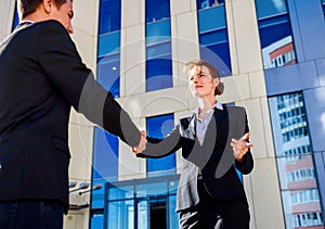 Professional business woman and man in formal suit shaking hands outdoors.