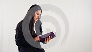 Professional business woman reading a book with a focused expression against a white background