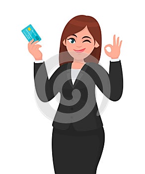 Professional business woman showing/holding credit/debit/ATM banking card and gesturing/making okay/ok sign, while winking eye.