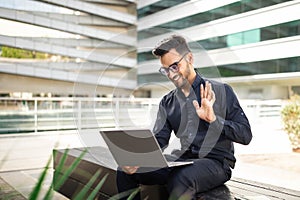 Professional businessman waves hello during video call on laptop outside