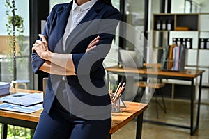 Professional businesswoman in formal business suit arms crossed and stands in her modern office