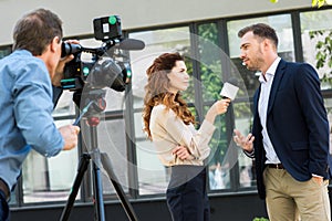 professional cameraman and journalist interviewing businessman near office