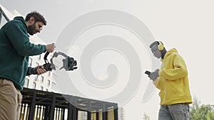 Professional cameraman takes video of african american man wearing headphones and yellow hoodie in courtyard of