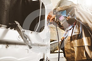 Professional car body repair, welding of auto body. Industrial worker welds metal elements of vehicle.