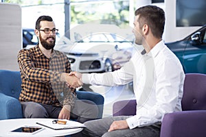 Professional car dealer shaking hands with buyer after transaction in the showroom