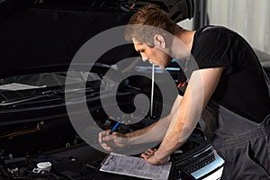 Professional car mechanic is examining engine under the hood at auto repair shop