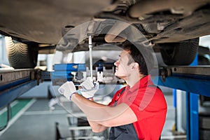 Professional car mechanic man working under lifted car in auto repair service