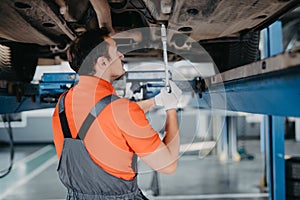 Professional car mechanic man working under lifted car in auto repair service