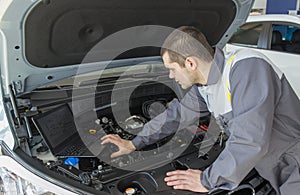 Professional car mechanic working in auto repair service with laptop