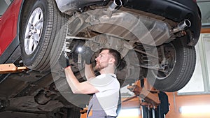 A professional car mechanic works under the king of a hoisting machine in a car repair shop.