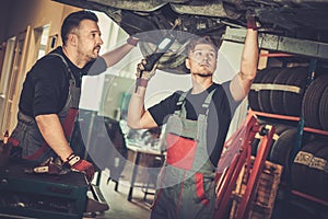 Professional car mechanics working under lifted car in auto repair service.