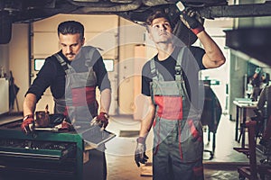 Professional car mechanics working under lifted car in auto repair service.