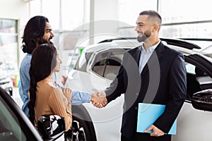 Professional Car Salesman Shaking Hands With Couple in a Showroom