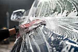 Professional car wash. Detailing worker washes the vehicle body with foam and rag.