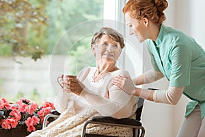 A professional caretaker in uniform helping a geriatric female p