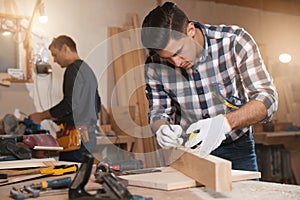 Professional carpenter and colleague working with plank in workshop
