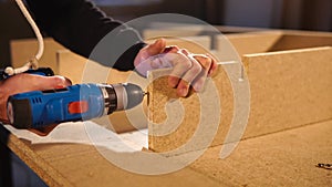 The professional carpenter makes holes in the particle board with a drill