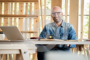 Professional carpenter man wearing glove and goggle sitting on the chair and looking foeward in the modern wood workplace. Many
