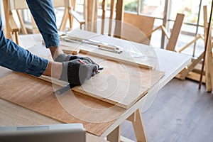 Professional carpenter man wearing glove using pencil and ruler to draw the line on the wood piece in the modern wood workplace.