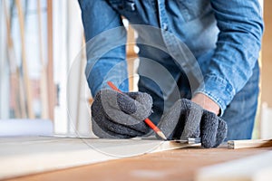 Professional carpenter wear glove and used pencil to point the line on the wooden sheet in the modern wood workplace. Create the