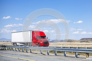 Professional carrier red big rig semi truck transporting cargo in dry van semi trailer running on the divided highway road in