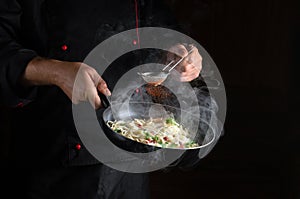 Professional chef adds spices to spaghetti in a steamed hot pan. Recipe or menu for restaurant or hotel on black background