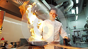 A professional chef in black gloves cooks in the restaurant kitchen in the Flambe style. Fruits and citrus fruits in a