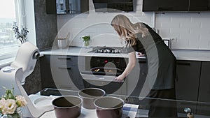Professional chef is cooking cake. Young attractive housewife opens oven on modern kitchen