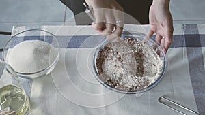 Professional chef is cooking cake. Young attractive housewife uses metal whisk to mix flour and cocoa in bowl