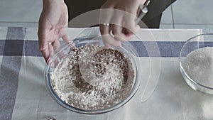 Professional chef is cooking cake. Young attractive housewife uses metal whisk to mix flour and cocoa in bowl