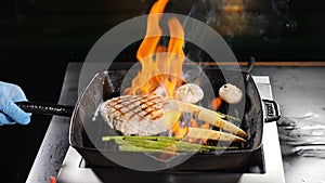 Professional chef cooking flambe style dish on restaurant kitchen. Igniting and stirring frying pan with flaming dish