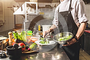 Professional chef cooking in the kitchen restaurant at the hotel, preparing dinner. A cook in an apron makes a salad of