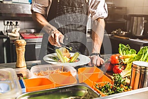 Professional chef cooking in the kitchen restaurant at the hotel, preparing dinner. A cook in an apron makes a salad of