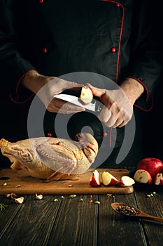 Professional chef cuts apples with a knife to add to raw duck before roasting in the oven. Cooking a national dish in the kitchen