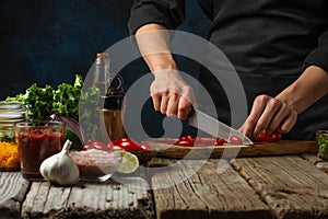 Professional chef cuts with knife cherry tomato on wooden chopped board for cooking tasty food for dinner. Backstage of preparing